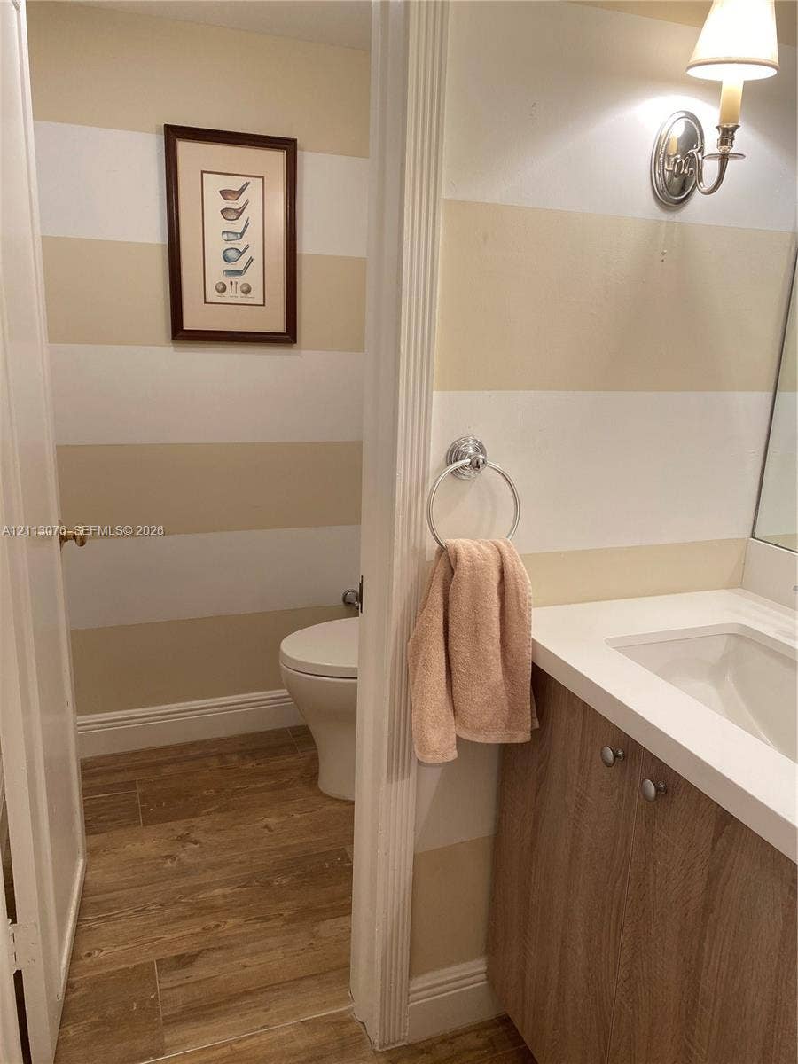 Bathroom featuring wood-finish flooring, a vanity with a white countertop and integrated sink, a wall-mounted light fixture, and a circular towel ring