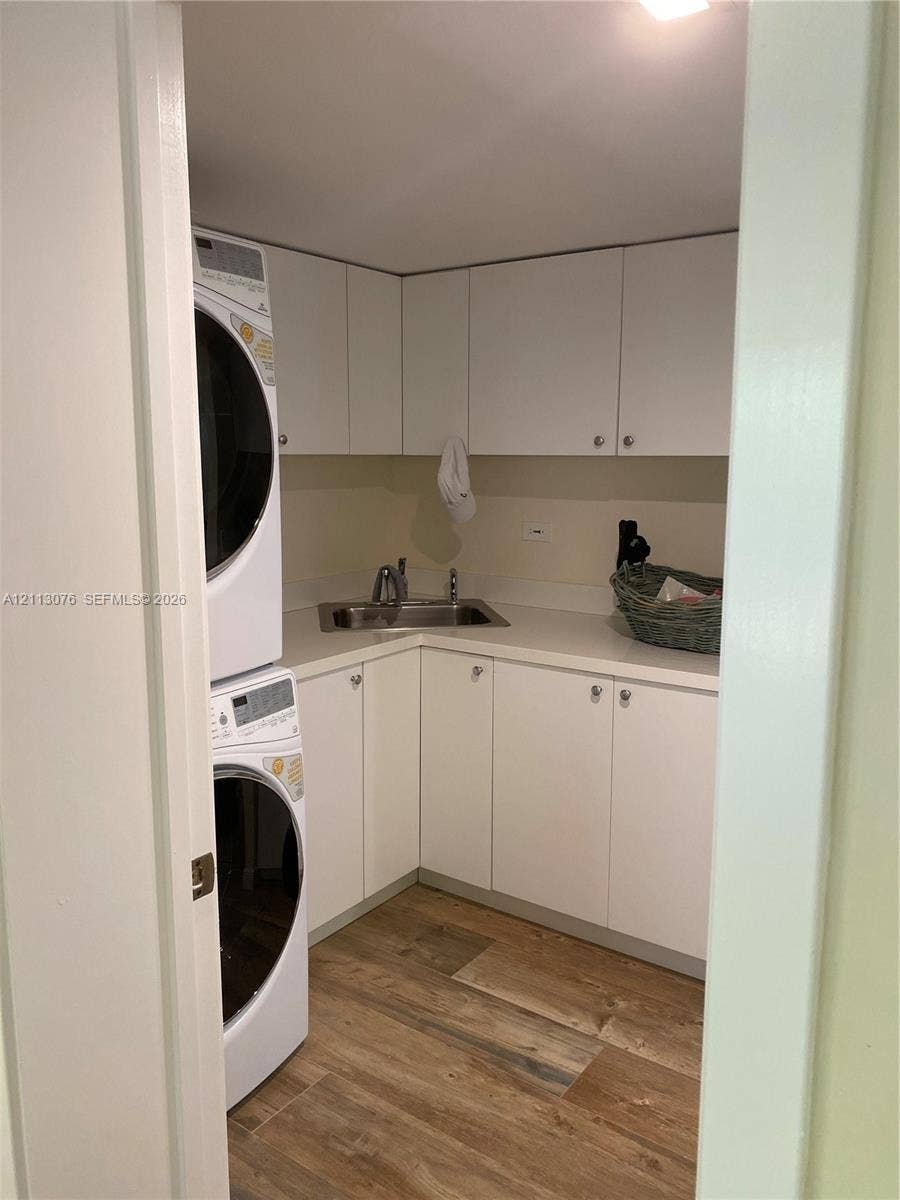 Laundry area featuring white cabinetry, solid-surface countertop, stainless steel sink with faucet, and wood-finish flooring