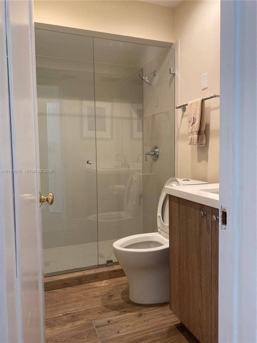 Bathroom featuring wood-finish flooring, a frameless glass shower enclosure, a vanity with a light-toned countertop, and chrome hardware