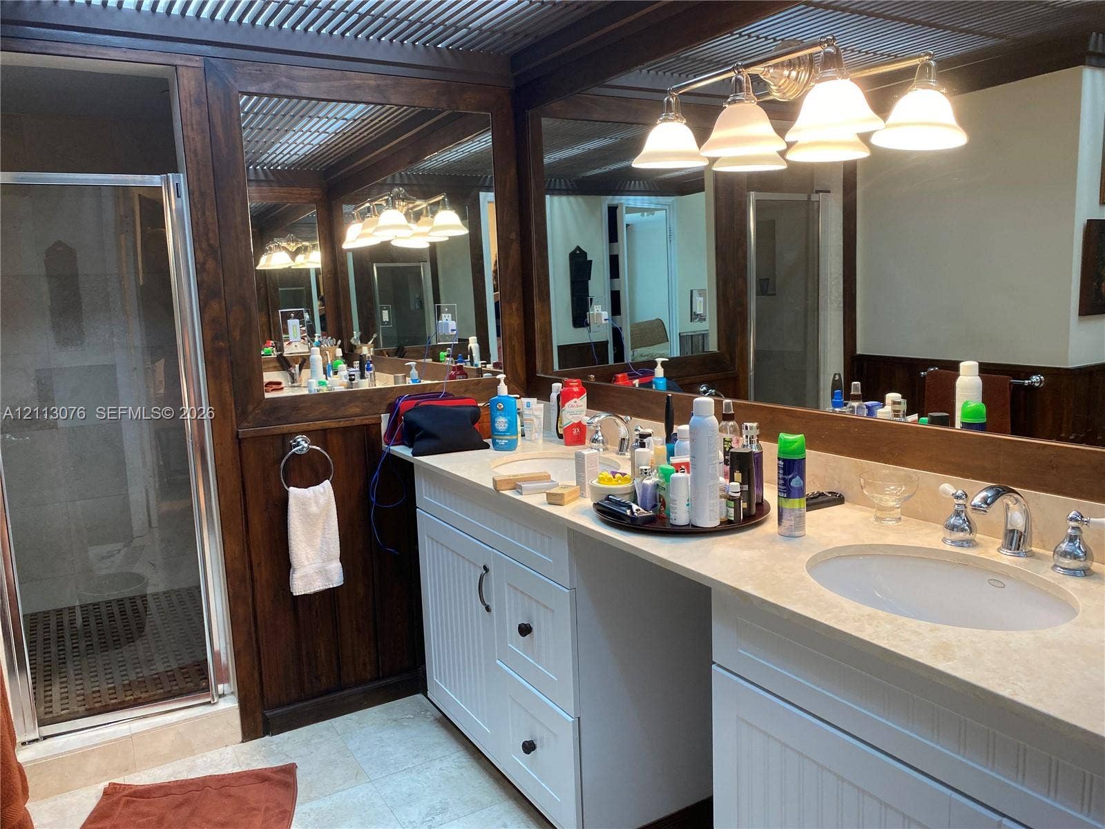 Dual-sink vanity with white cabinetry, stone-finish countertops, wall-to-wall mirrors with wood-trim, a glass-enclosed shower, and multi-light vanity fixtures