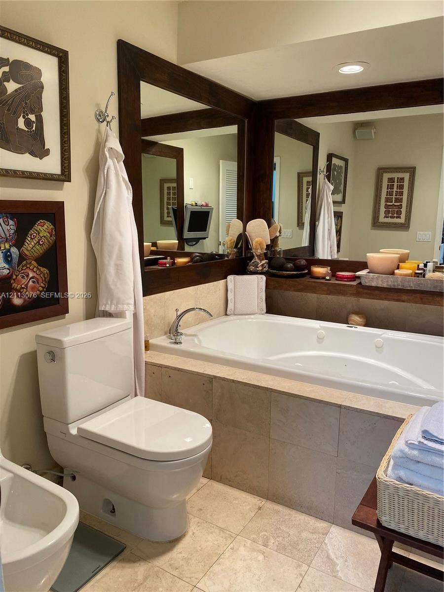Jetted soaking tub with tile surround, dual wall-mounted mirrors with stained wood framing, and recessed ceiling lighting