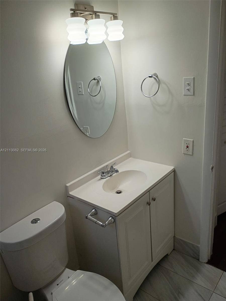 2222 Fillmore Street, #105, Hollywood, Hollywood, FL 33020 Bathroom featuring a white vanity cabinet with a integrated basin, oval wall-mounted mirror, three-light fixture, and stone-finish tile flooring