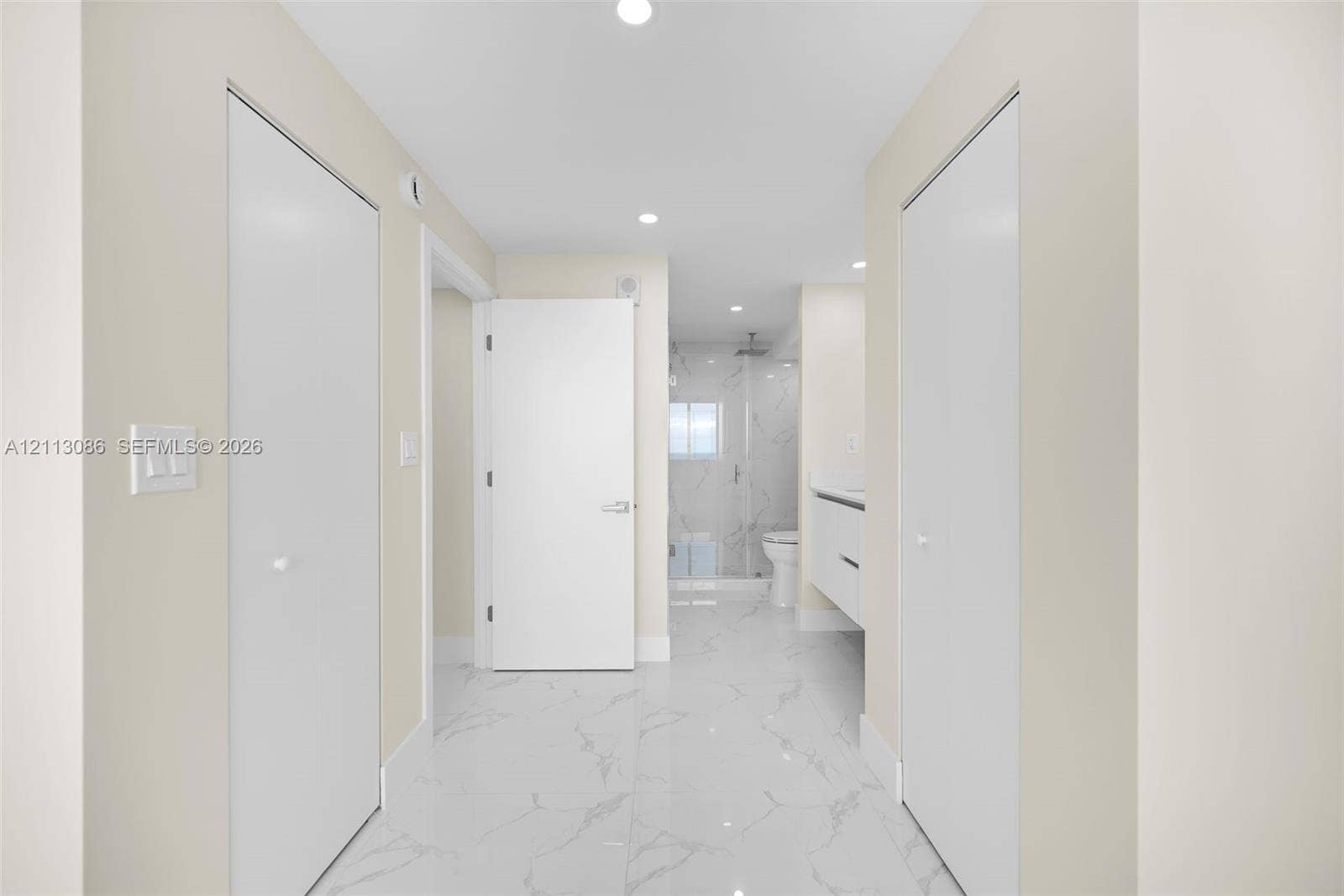 7135 Collins Avenue, #1632, Miami Beach, FL 33141 Hallway featuring high-gloss, large-format veined tile flooring, recessed ceiling lighting, dual floor-to-ceiling closets with white doors, and a modern wall-mounted floating vanity