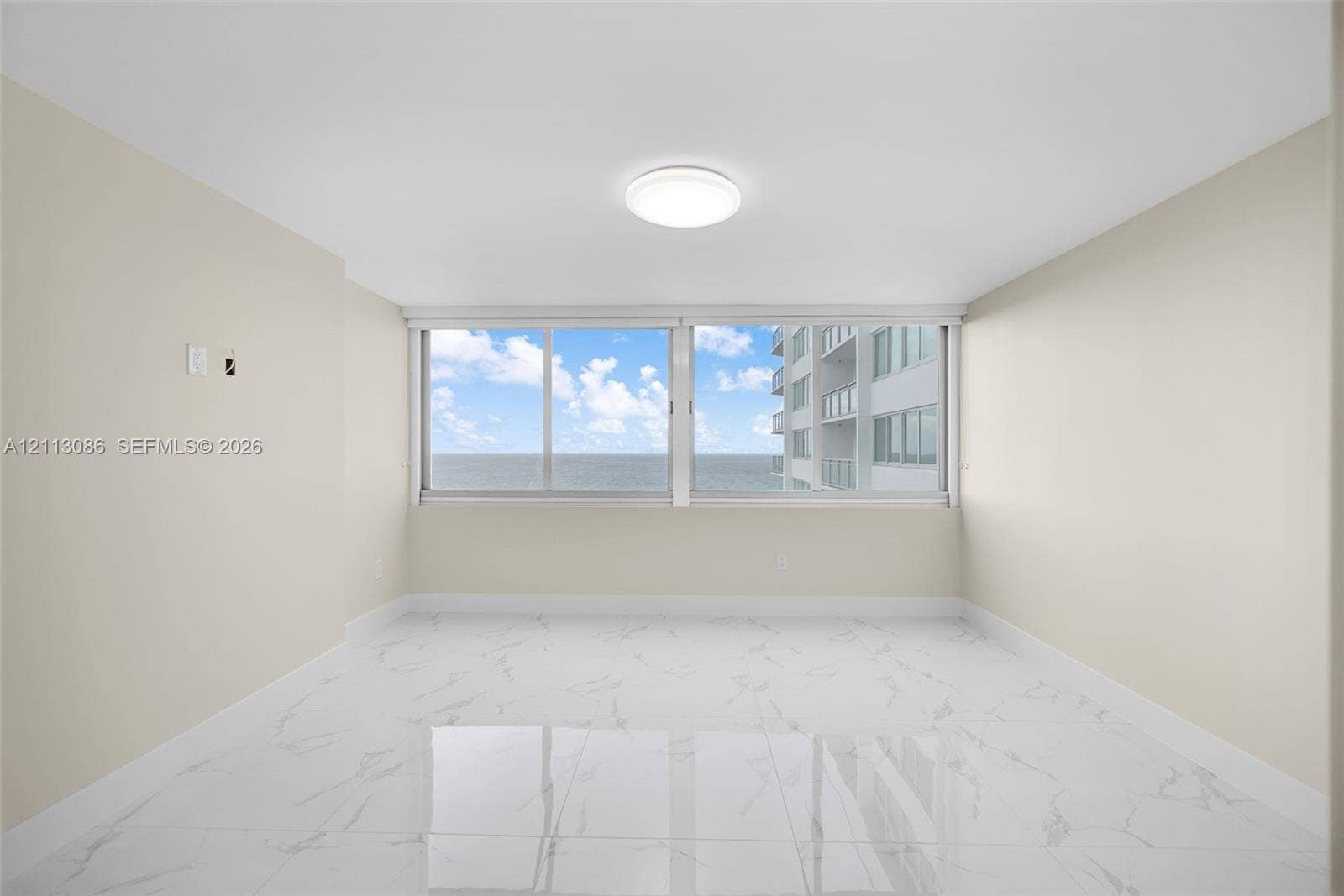 7135 Collins Avenue, #1632, Miami Beach, FL 33141 Spacious interior featuring white tile flooring with grey veining, neutral wall tones, large-format sliding windows, and flush-mount ceiling lighting