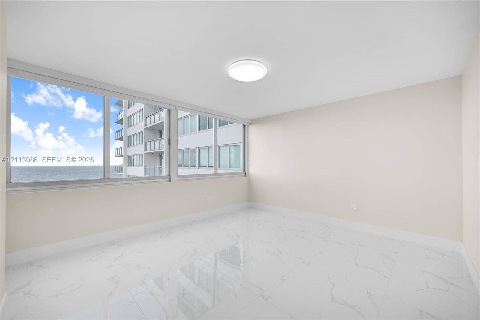 7135 Collins Avenue, #1632, Miami Beach, FL 33141 Expansive interior space featuring large-format stone-finish tile flooring, floor-to-ceiling windows, and a flush-mount overhead light fixture