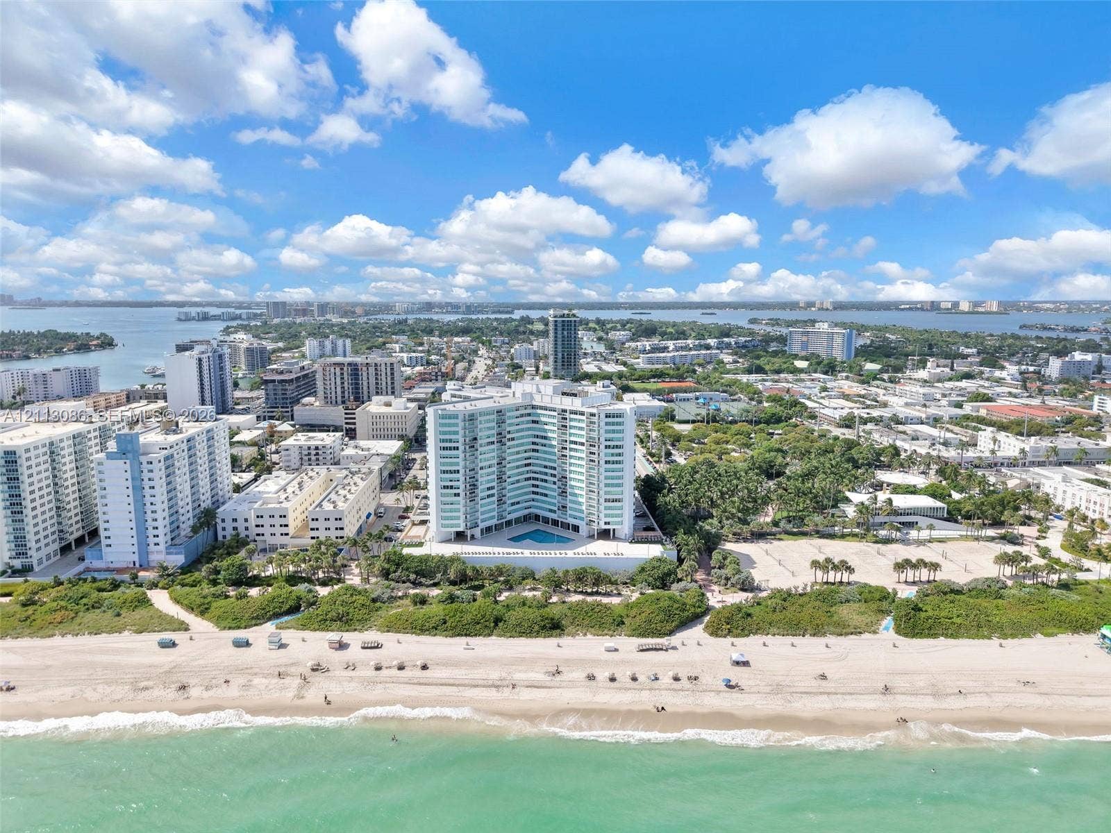7135 Collins Avenue, #1632, Miami Beach, FL 33141 High-rise building featuring a curved architectural design, expansive oceanfront proximity, ground-level outdoor swimming pool, and direct access to sandy beach terrain