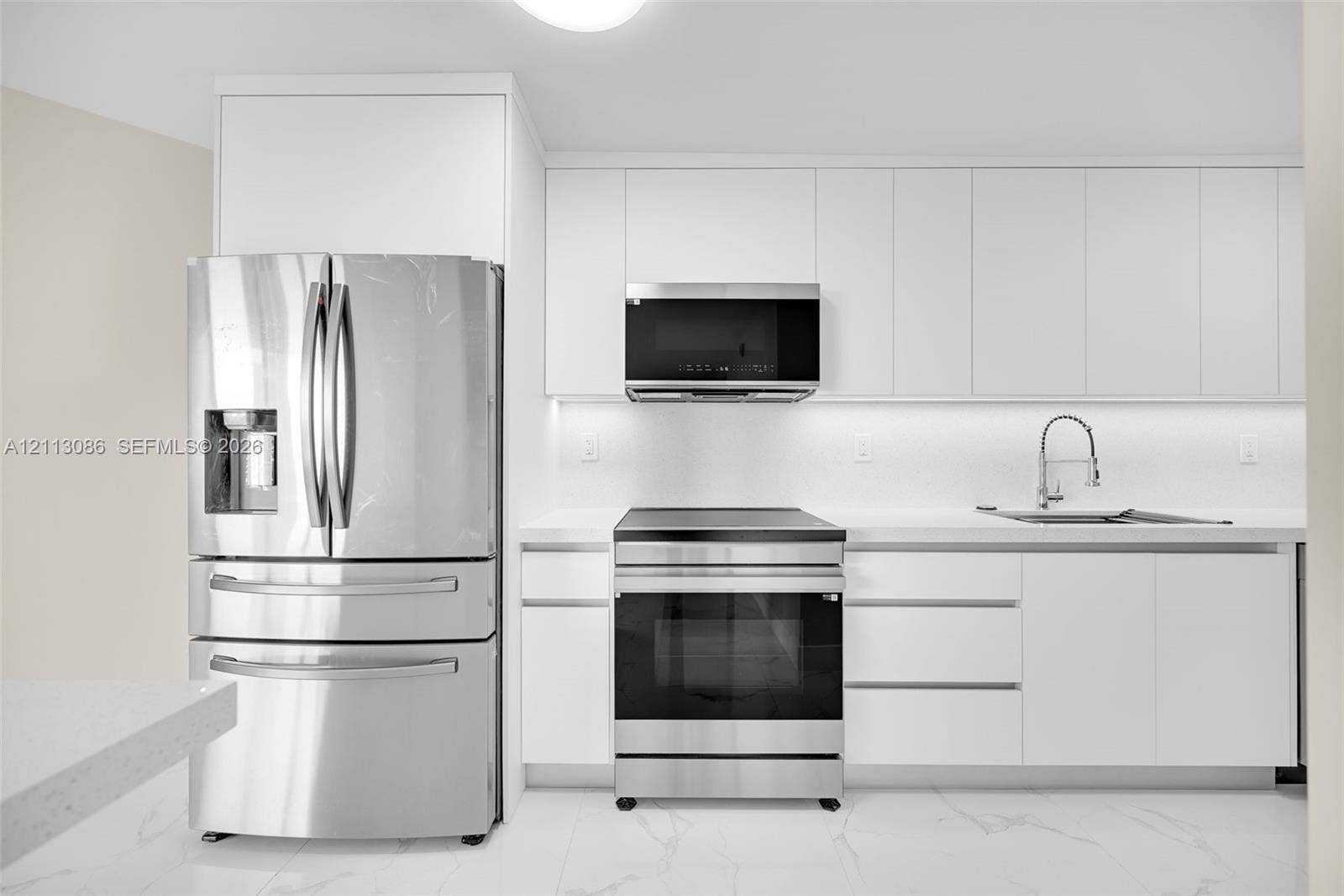 7135 Collins Avenue, #1632, Miami Beach, FL 33141 Minimalist kitchen featuring matte white flat-panel cabinetry, stainless steel appliances, a high-arc pull-down faucet, and light stone-patterned flooring