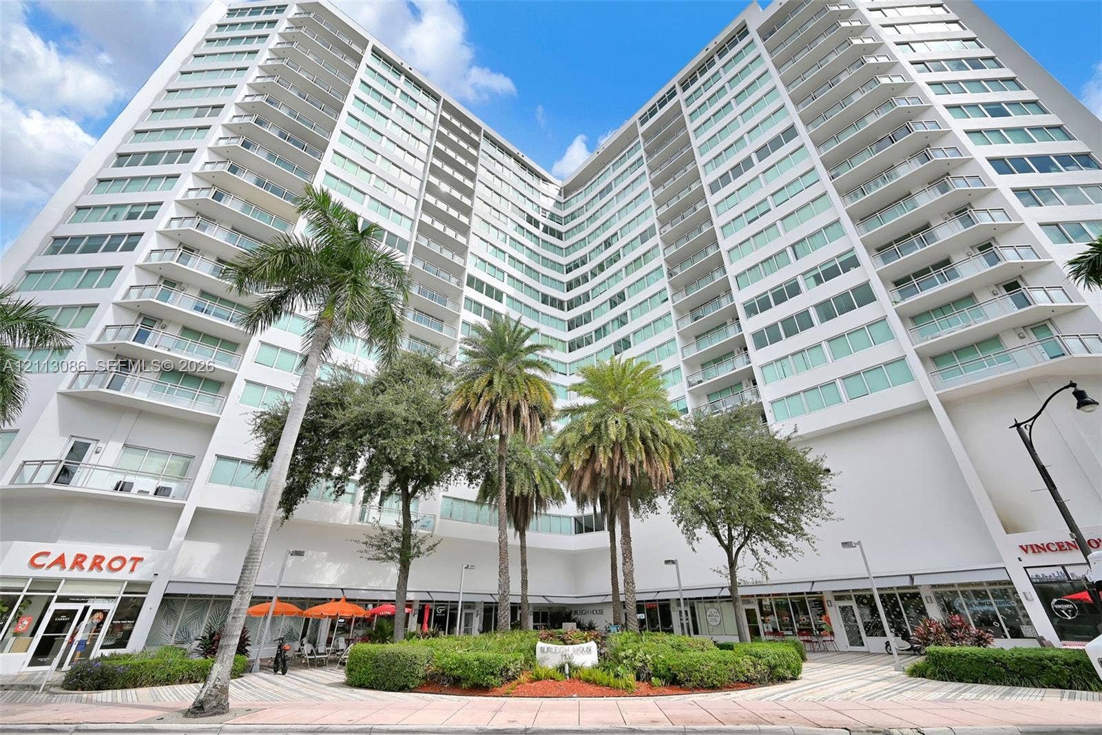 7135 Collins Avenue, #1632, Miami Beach, FL 33141 High-rise concrete exterior featuring expansive glass windows and private balconies, complemented by ground-level commercial frontage and manicured landscaping with mature palm trees
