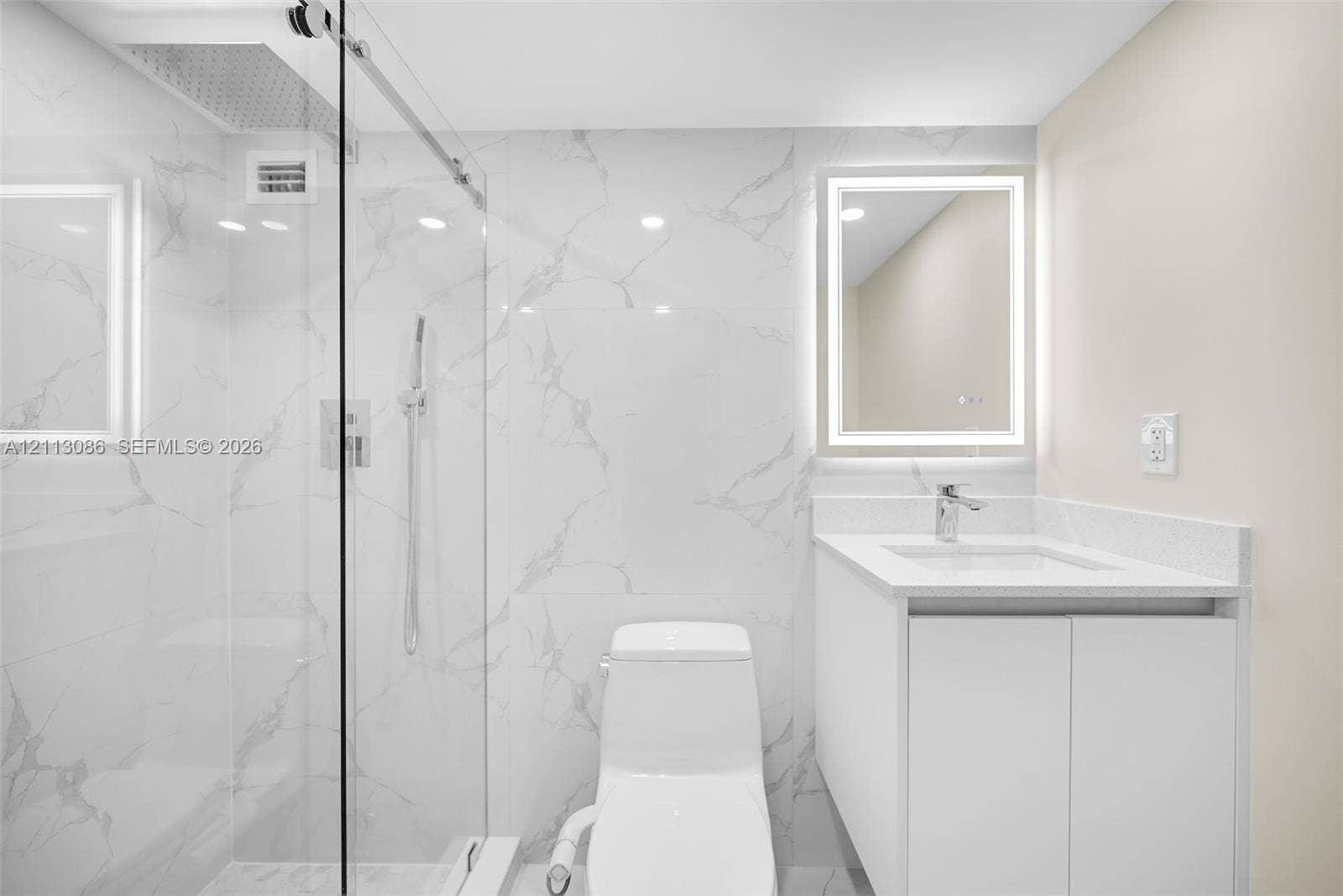 7135 Collins Avenue, #1632, Miami Beach, FL 33141 Walk-in shower with floor-to-ceiling large-format tile, frameless glass enclosure, wall-mounted vanity with integrated sink, and illuminated mirror
