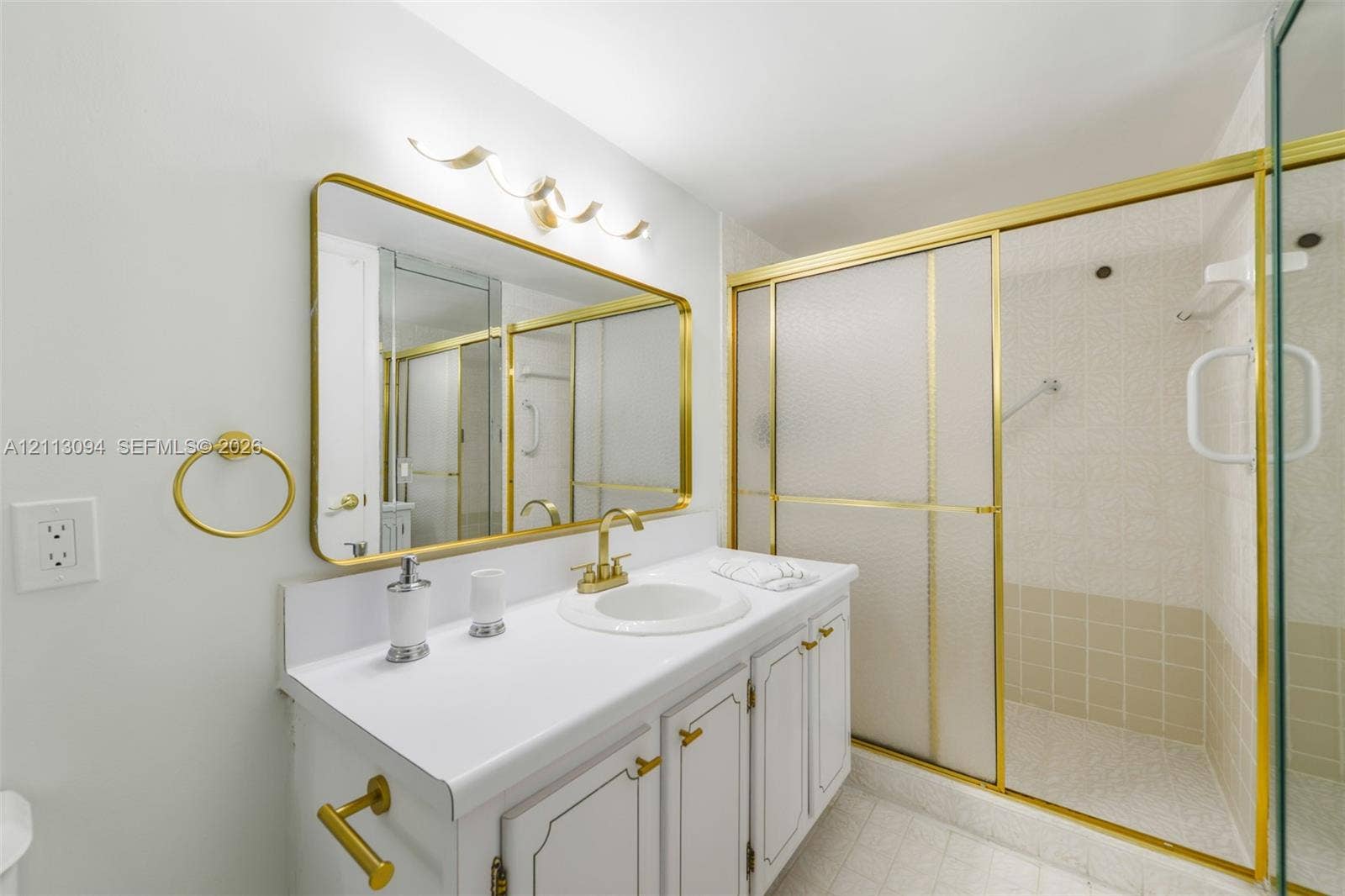Bathroom vanity with a white countertop, inset sink, brass-tone hardware, and an expansive wall-mounted mirror