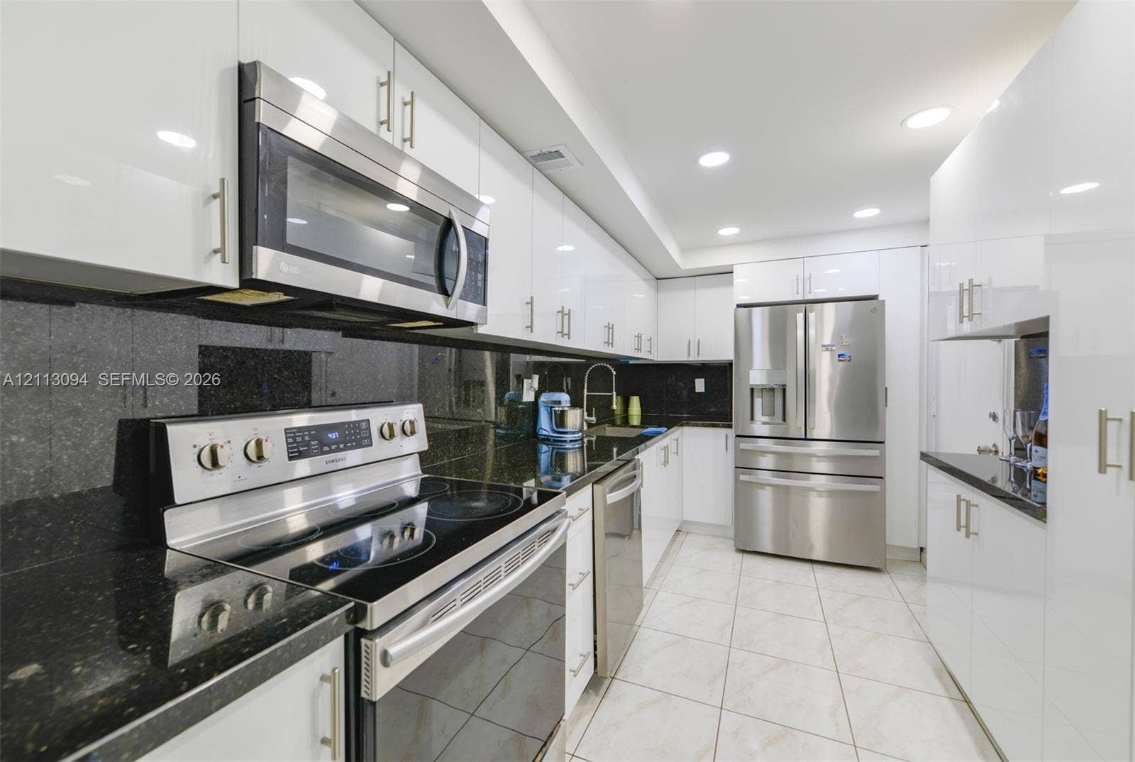 Kitchen featuring high-gloss white cabinetry, dark stone countertops, stainless steel appliances, tile flooring, and recessed ceiling lighting