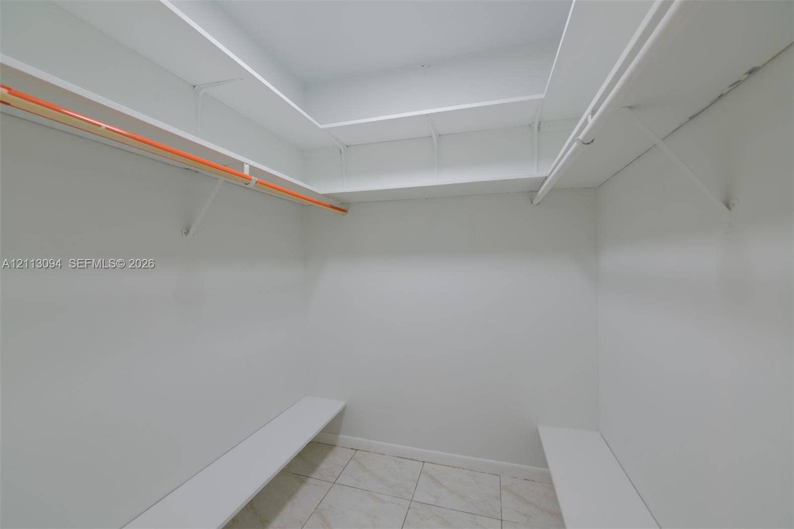 Walk-in storage space featuring custom multi-level shelving, integrated hanging rods, and tile flooring