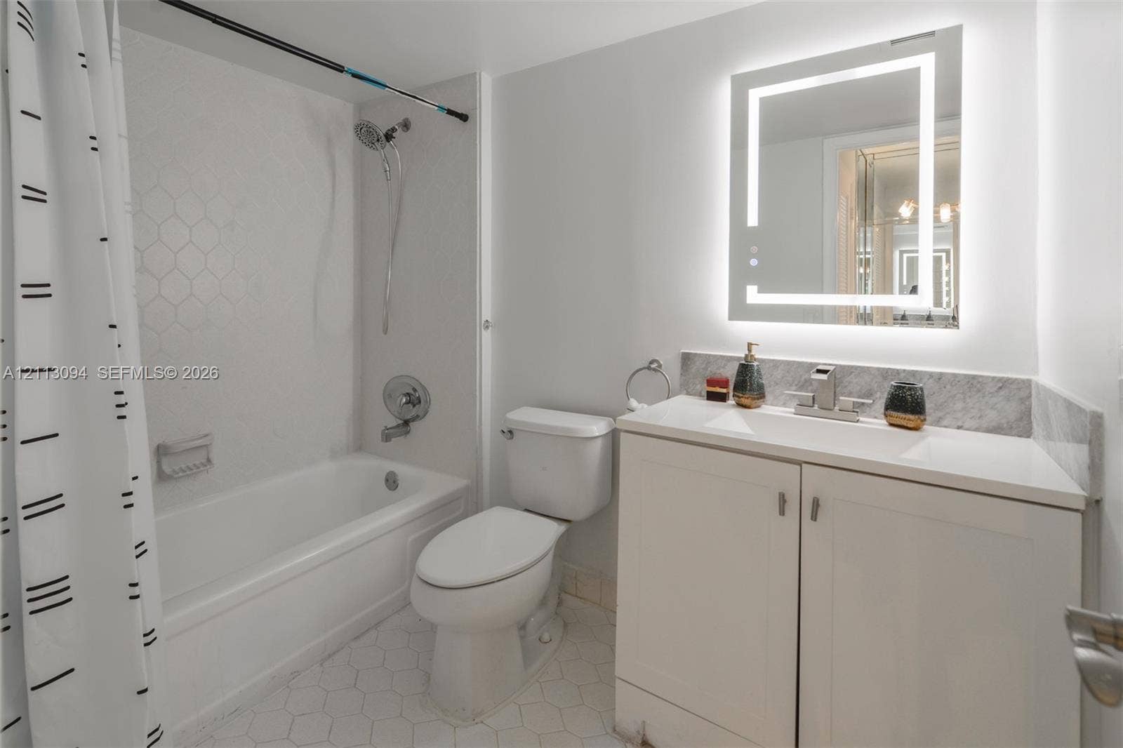 Bathroom featuring a white vanity cabinet with a stone-top integrated sink, a rectangular backlit mirror, and a tiled shower enclosure with a geometric pattern