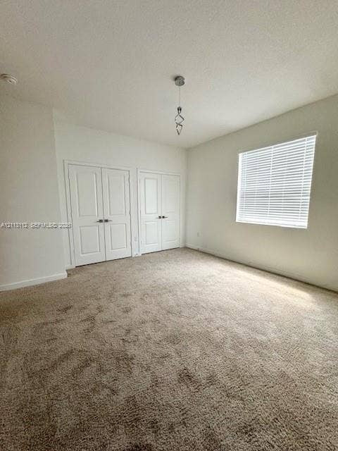 557 NE 5th Terrace, Florida City, Florida City, FL 33034 Interior space featuring neutral-toned carpeting, two sets of panel doors with metallic hardware, a single geometric pendant light fixture, and a window with horizontal blinds