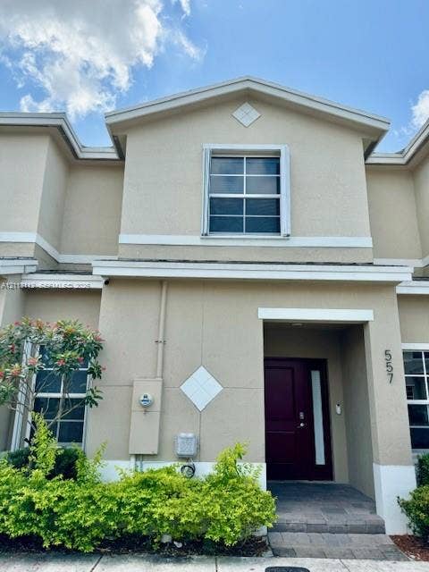 557 NE 5th Terrace, Florida City, Florida City, FL 33034 Exterior featuring a stucco facade, dark-toned entry door with a vertical glass panel, gabled roofline, decorative diamond-shaped wall accents, and paved entry path