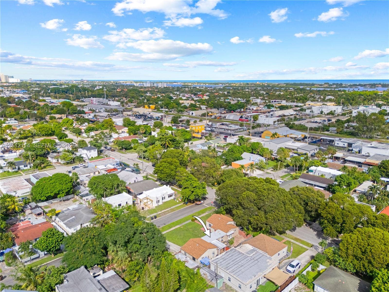 Aerial perspective of a detached residential property featuring a shingle roof, paved driveway, and grass lawn within a developed neighborhood setting