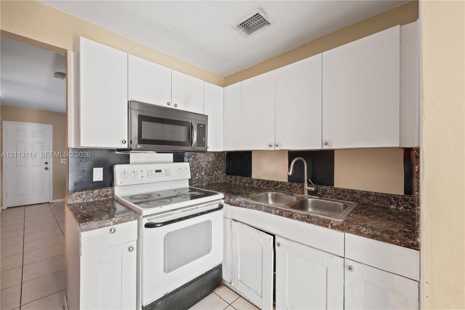 Kitchen featuring white cabinetry, stone-finish countertops, stainless steel microwave, white electric range, and a dual-basin stainless steel sink with a high-arch faucet
