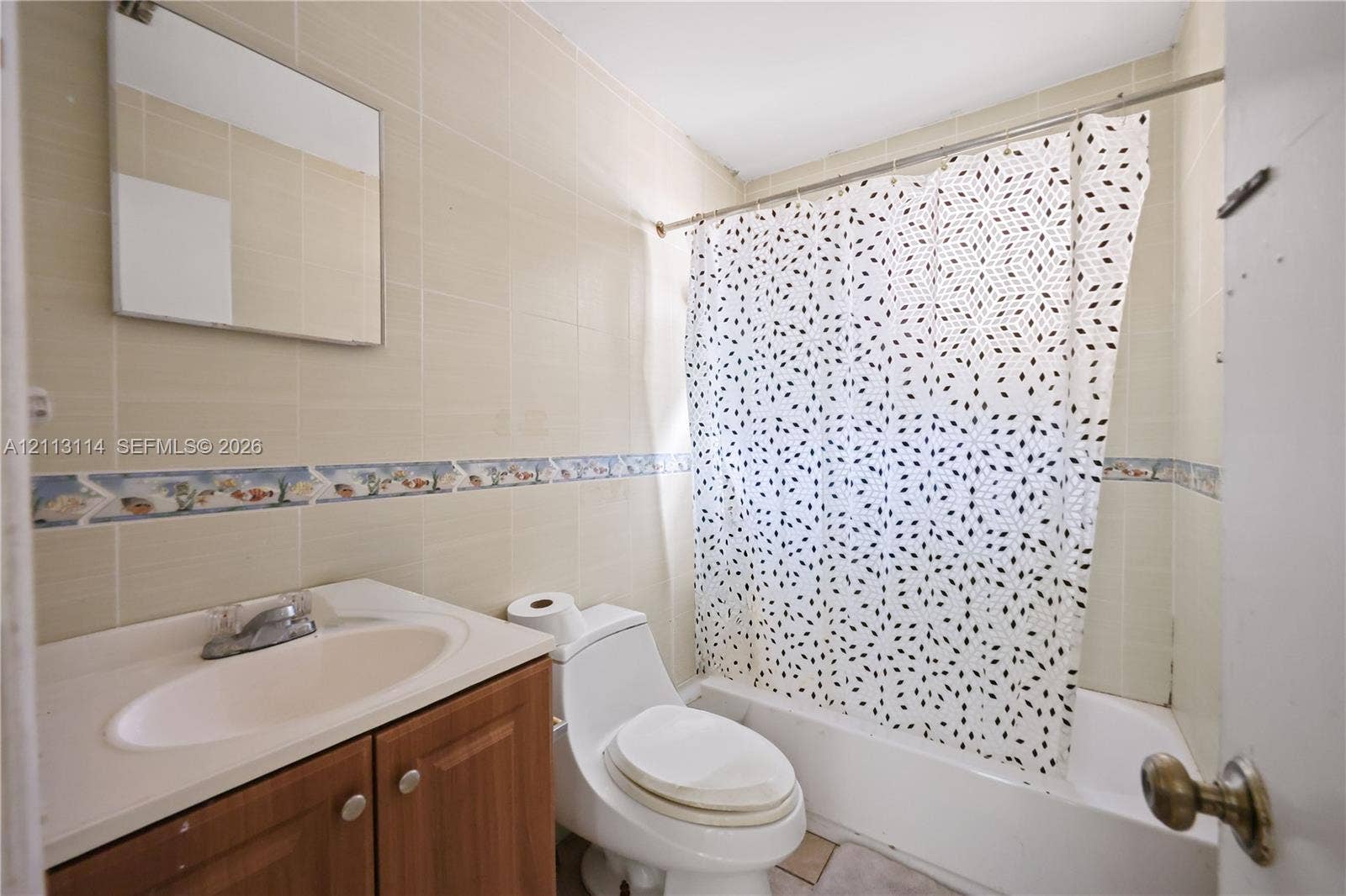 Bathroom featuring wall-to-wall tiling, a wood-finish vanity with an integrated sink, a full-width vanity mirror, and a combination tub and shower
