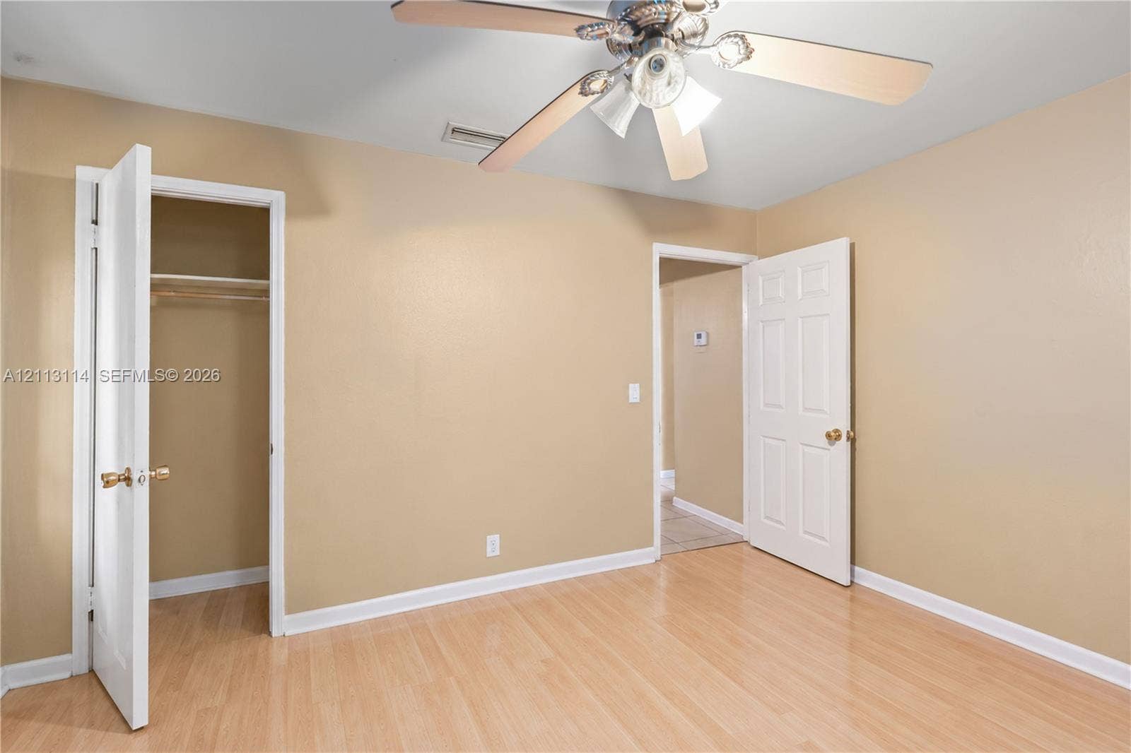 Neutral-toned interior room featuring wood-finish flooring, a multi-blade ceiling fan with integrated lighting, and a reach-in closet with built-in shelving