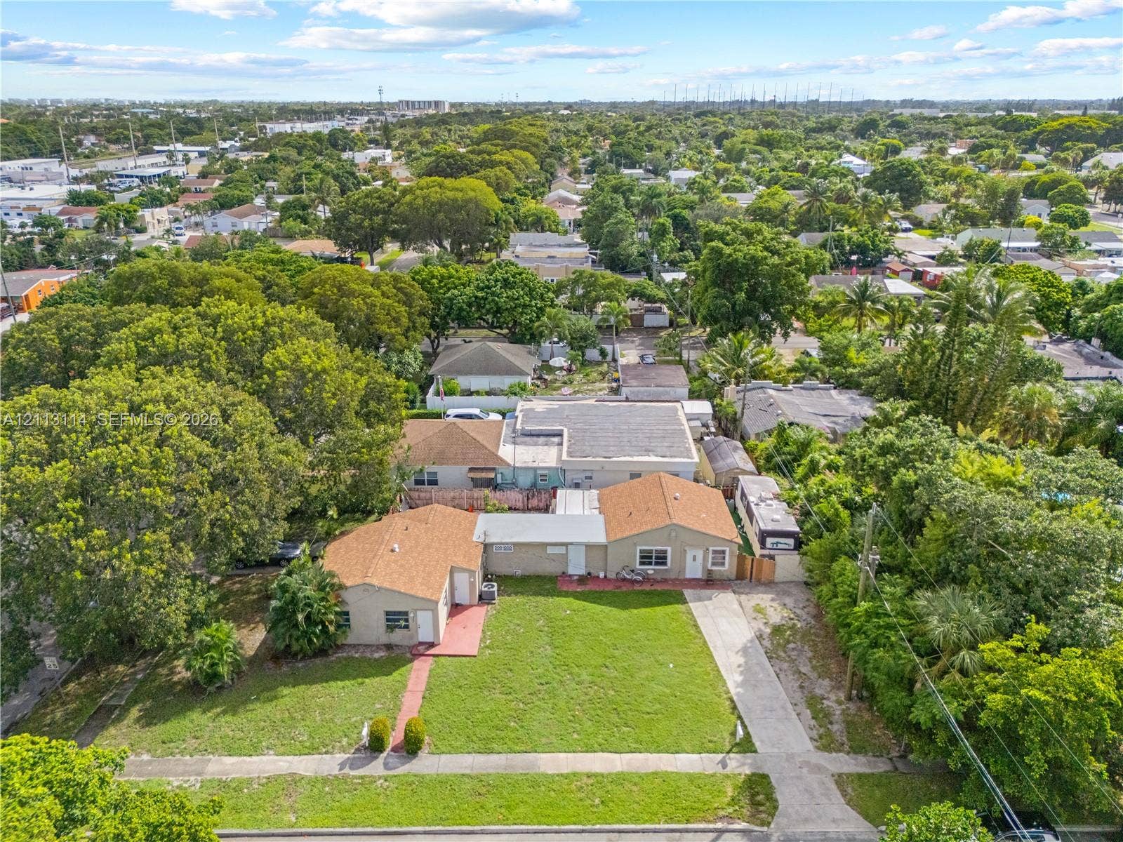 Expansive corner lot featuring a concrete driveway, multi-building structure with shingle roofing, and established mature landscaping