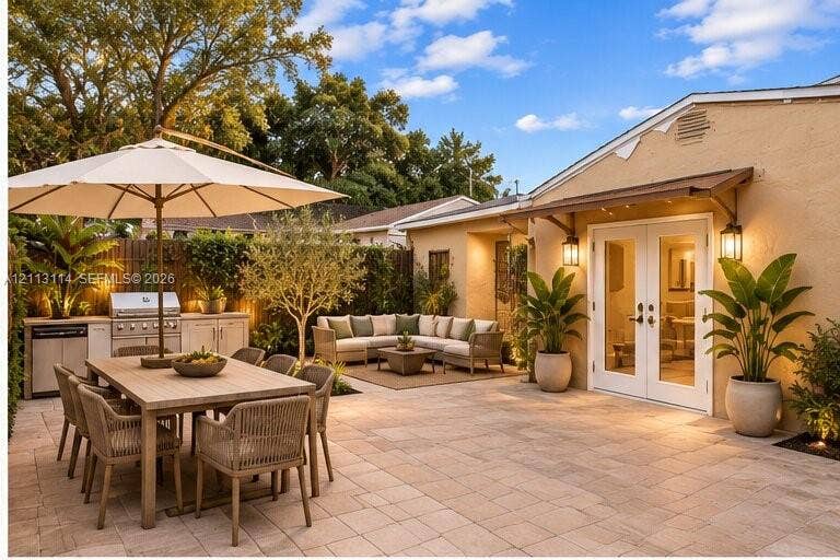 AI-generated photo of the spacious paved patio featuring an integrated outdoor kitchen, stainless steel grill, attached wall-mounted lighting, and double-door entry