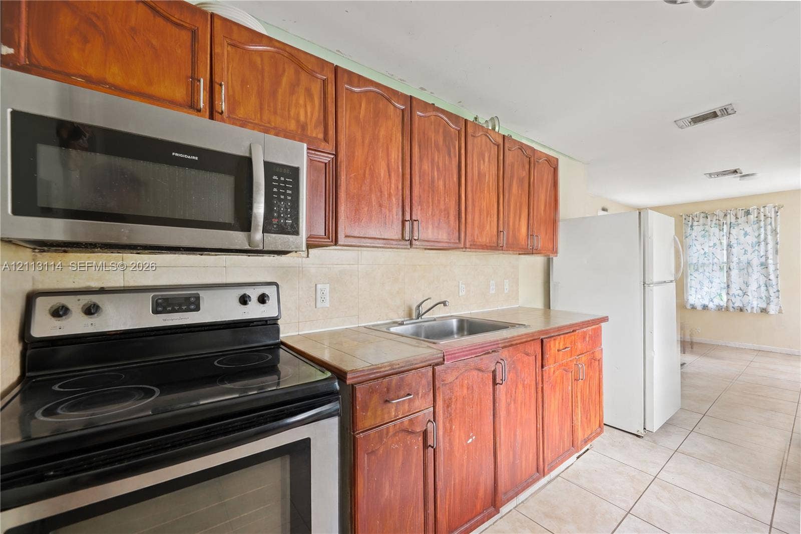 Kitchen featuring stained wood cabinetry, tile countertops, stainless steel microwave, black electric range, and ceramic tile flooring
