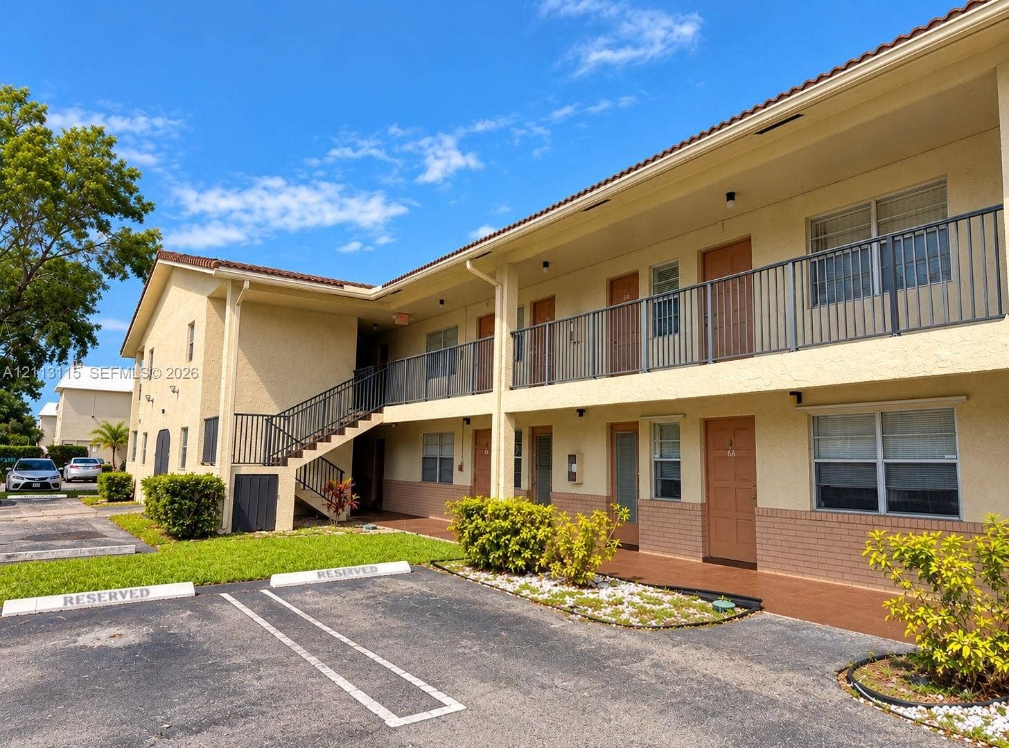 8705 NW 38th Drive, #4A, Coral Springs, Coral Springs, FL 33065 Stucco exterior facade featuring a tiled roof, metal balcony railings, and exterior stairwell access with ground-level parking