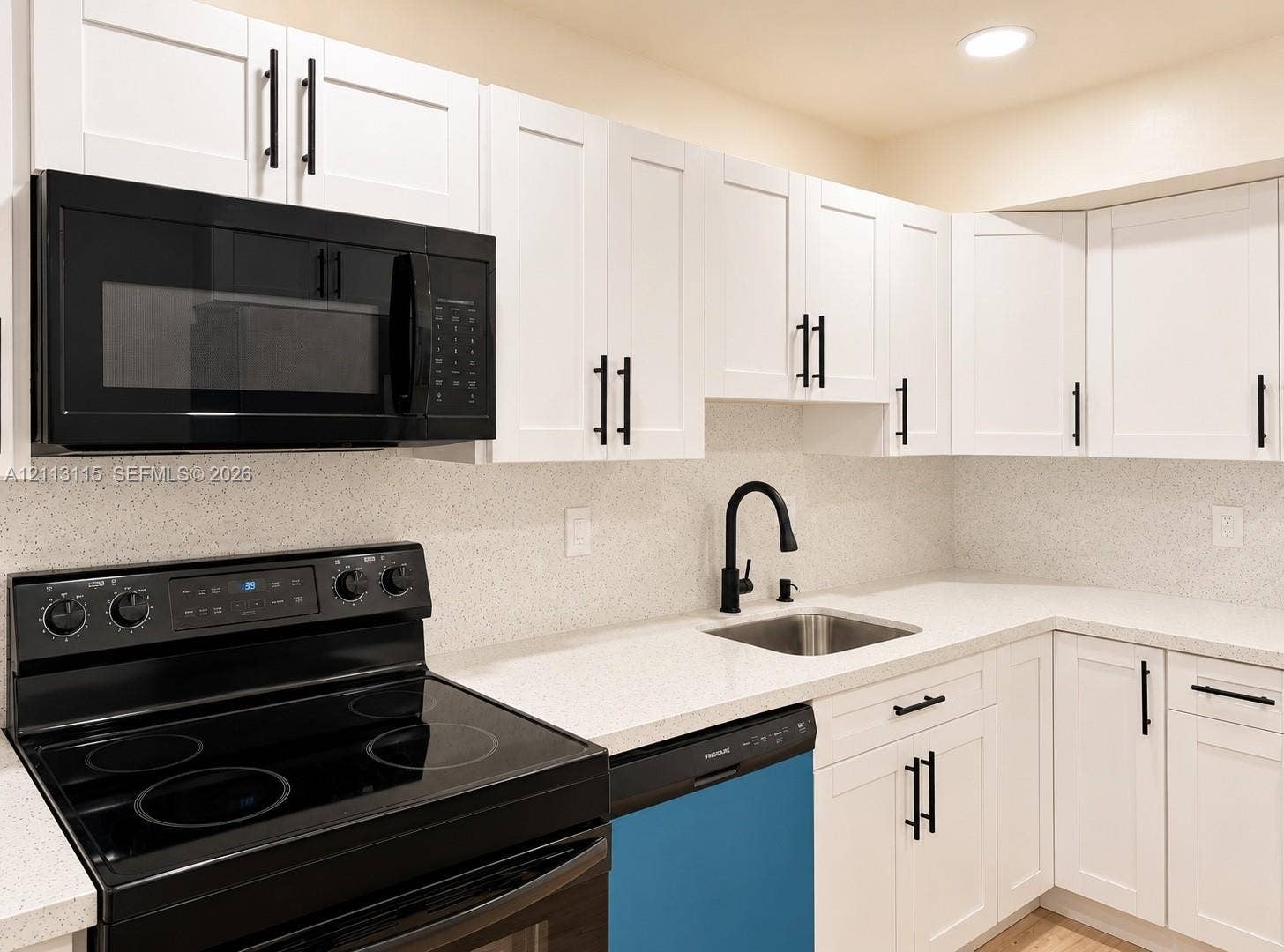8705 NW 38th Drive, #4A, Coral Springs, Coral Springs, FL 33065 Kitchen featuring white shaker-style cabinetry, solid-surface countertops, black finish hardware, a stainless steel undermount sink with a matte black faucet, and a black appliance suite