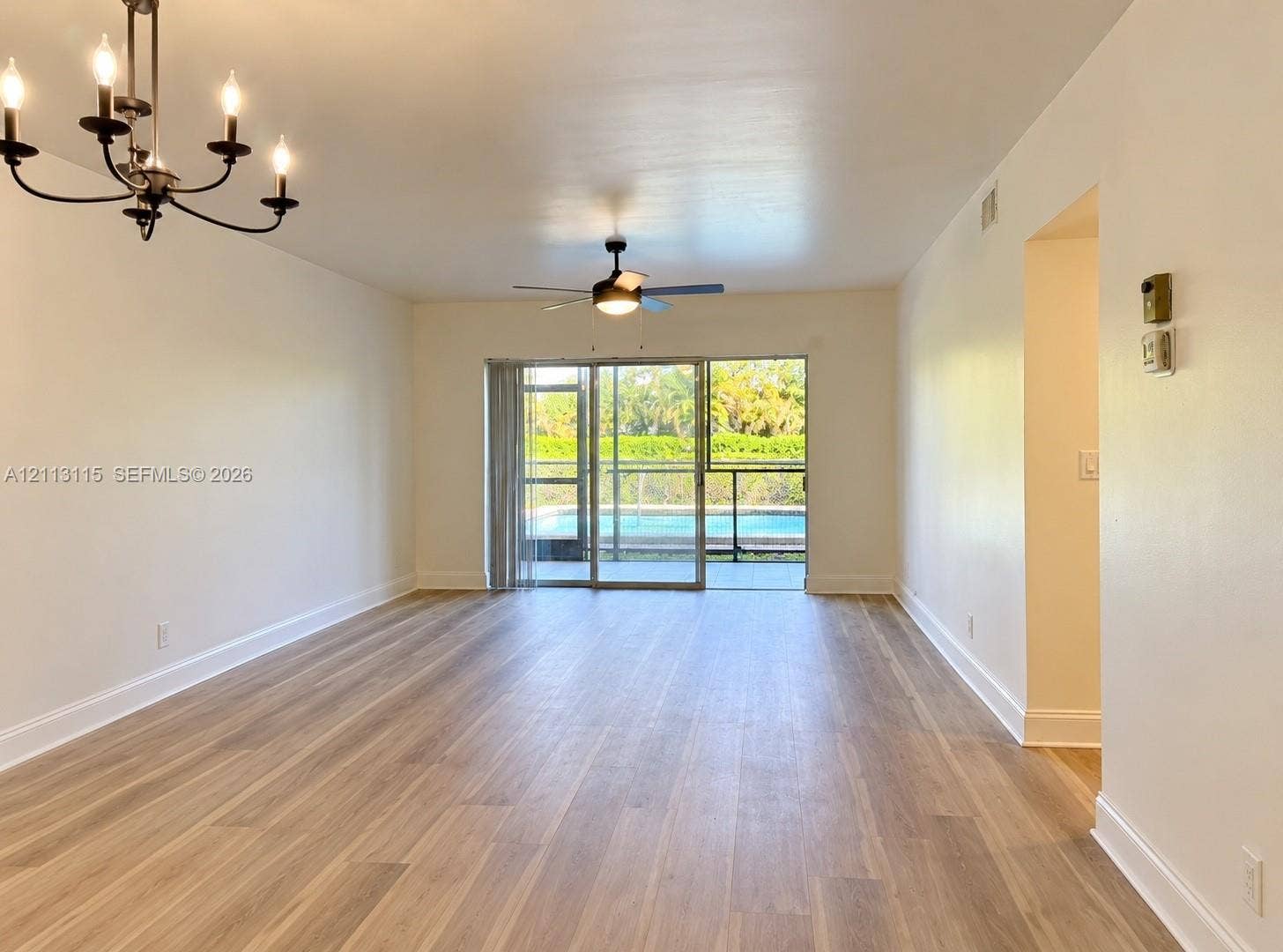 8705 NW 38th Drive, #4A, Coral Springs, Coral Springs, FL 33065 Open-concept interior featuring light wood-finish flooring, a multi-arm iron chandelier, a ceiling fan, and large sliding glass doors providing outdoor access
