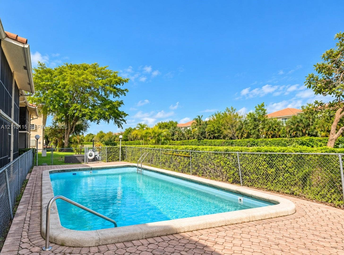 8705 NW 38th Drive, #4A, Coral Springs, Coral Springs, FL 33065 In-ground swimming pool featuring a concrete deck, metal handrail, chain-link perimeter fencing, and mature landscaping