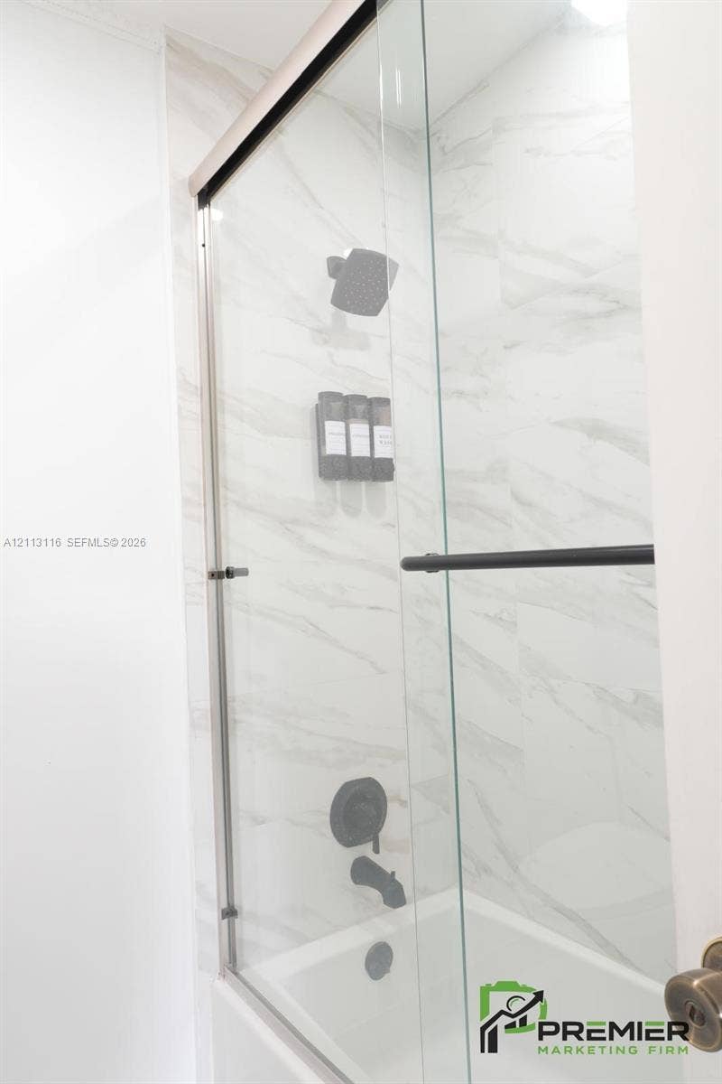 4341 NW 178th Drive, Miami Gardens, FL 33055 Shower enclosure featuring large-format tile surround, glass sliding door, and matte black shower fixtures