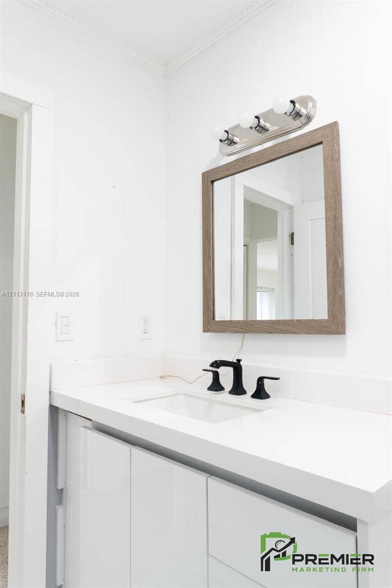 4341 NW 178th Drive, Miami Gardens, FL 33055 Glossy white vanity featuring a solid surface countertop, undermount sink, matte black widespread faucet, wood-toned framed mirror, and a three-light vanity fixture