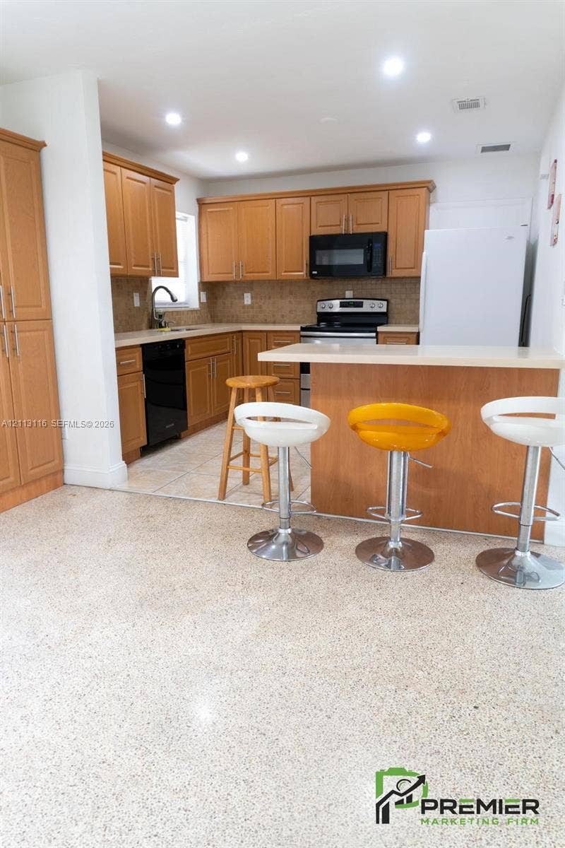 4341 NW 178th Drive, Miami Gardens, FL 33055 Kitchen featuring medium-tone wood cabinetry, solid-surface countertops, tile flooring, and a breakfast bar