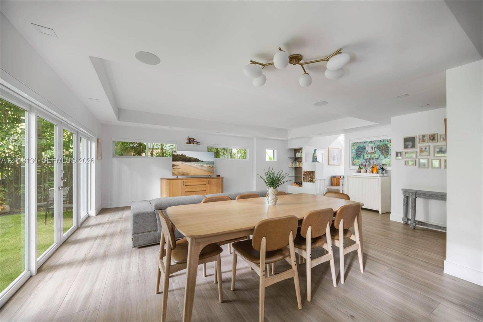 Open-concept living space featuring wood-finish flooring, multi-panel glass sliding doors, recessed ceiling lighting, clerestory windows, and a multi-globe chandelier