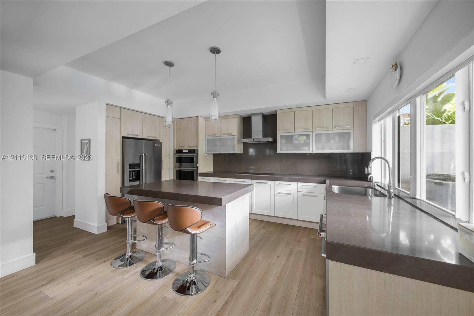 Kitchen featuring wood-finish cabinetry, stone countertops, stainless steel appliances, double wall ovens, and dual pendant lighting