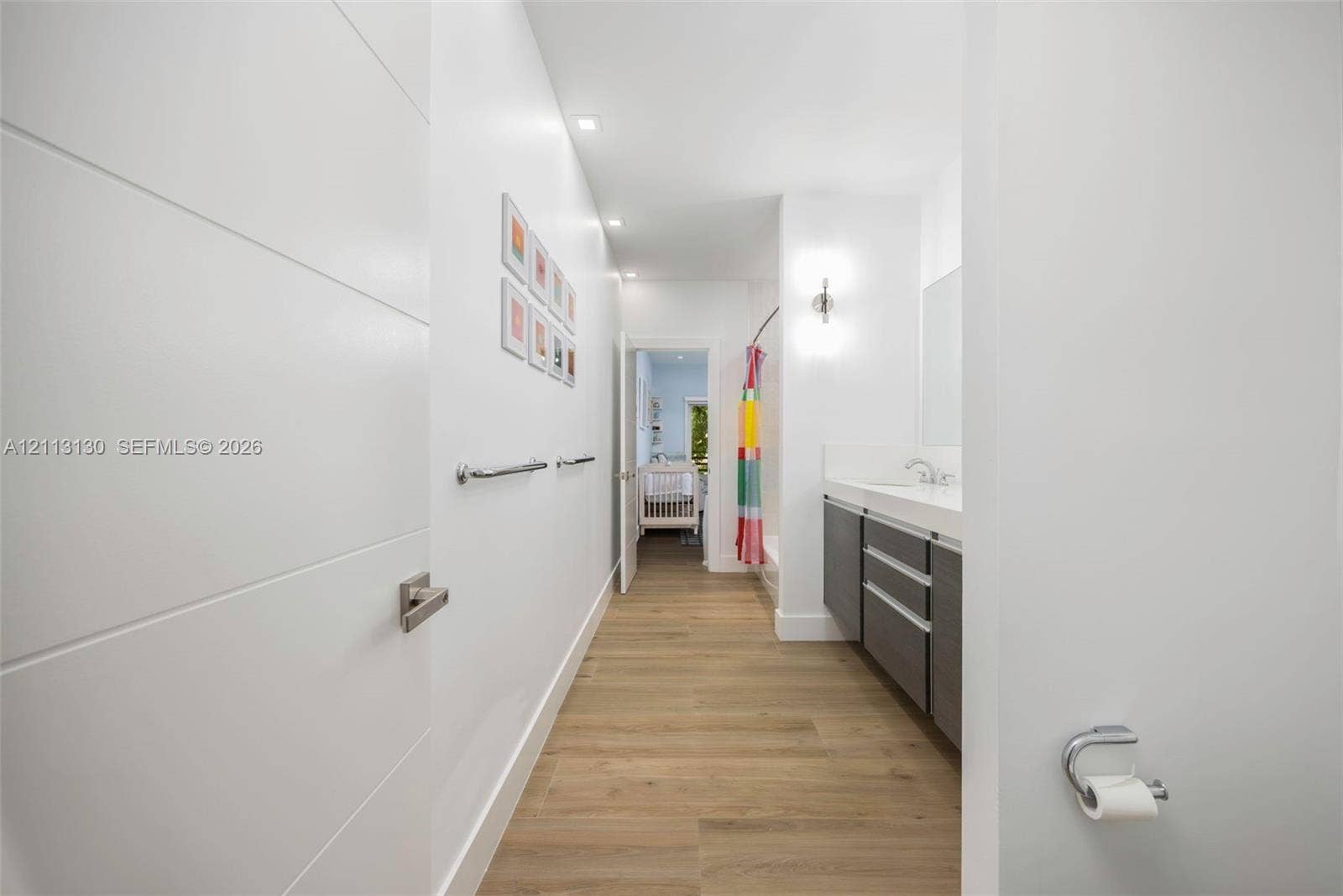 Bathroom featuring wood-finish flooring, a floating vanity with a light-toned countertop, integrated dual-basin sink, recessed lighting, and wall-mounted vanity sconces