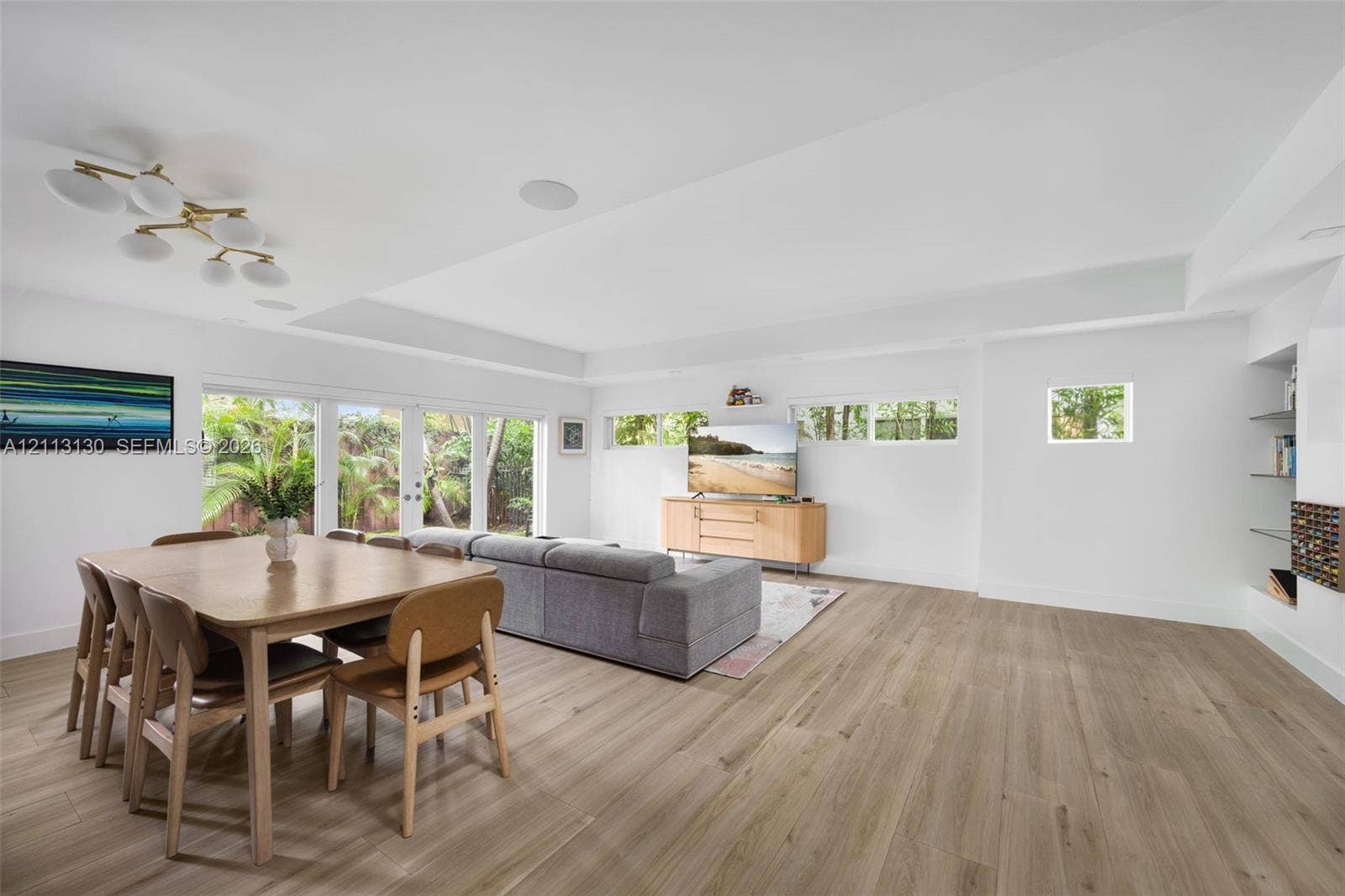 Open-concept interior featuring wood-finish flooring, recessed lighting, multi-panel glass exterior doors, clerestory windows, and built-in glass shelving