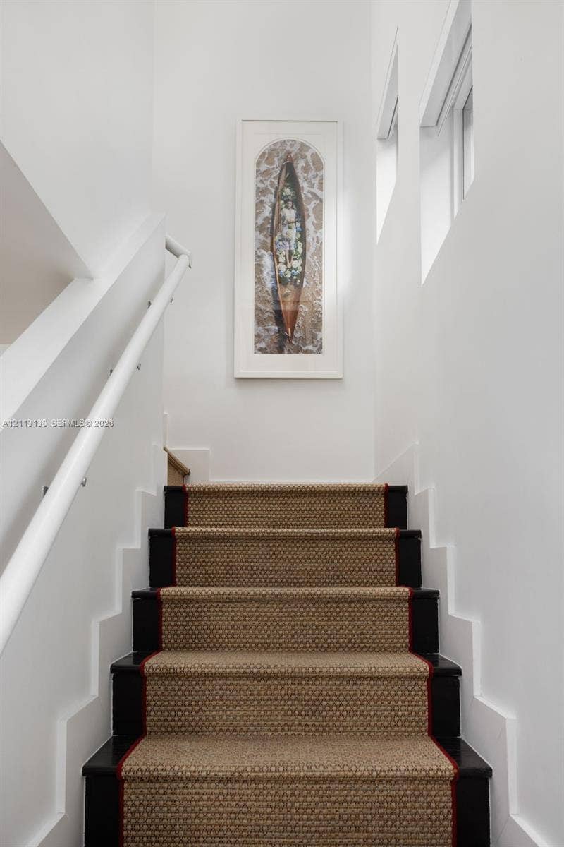 Staircase featuring dark-finished wooden treads, textured stair runner with a bordered edge, white wall-mounted handrail, and high-reaching walls with geometric moulding