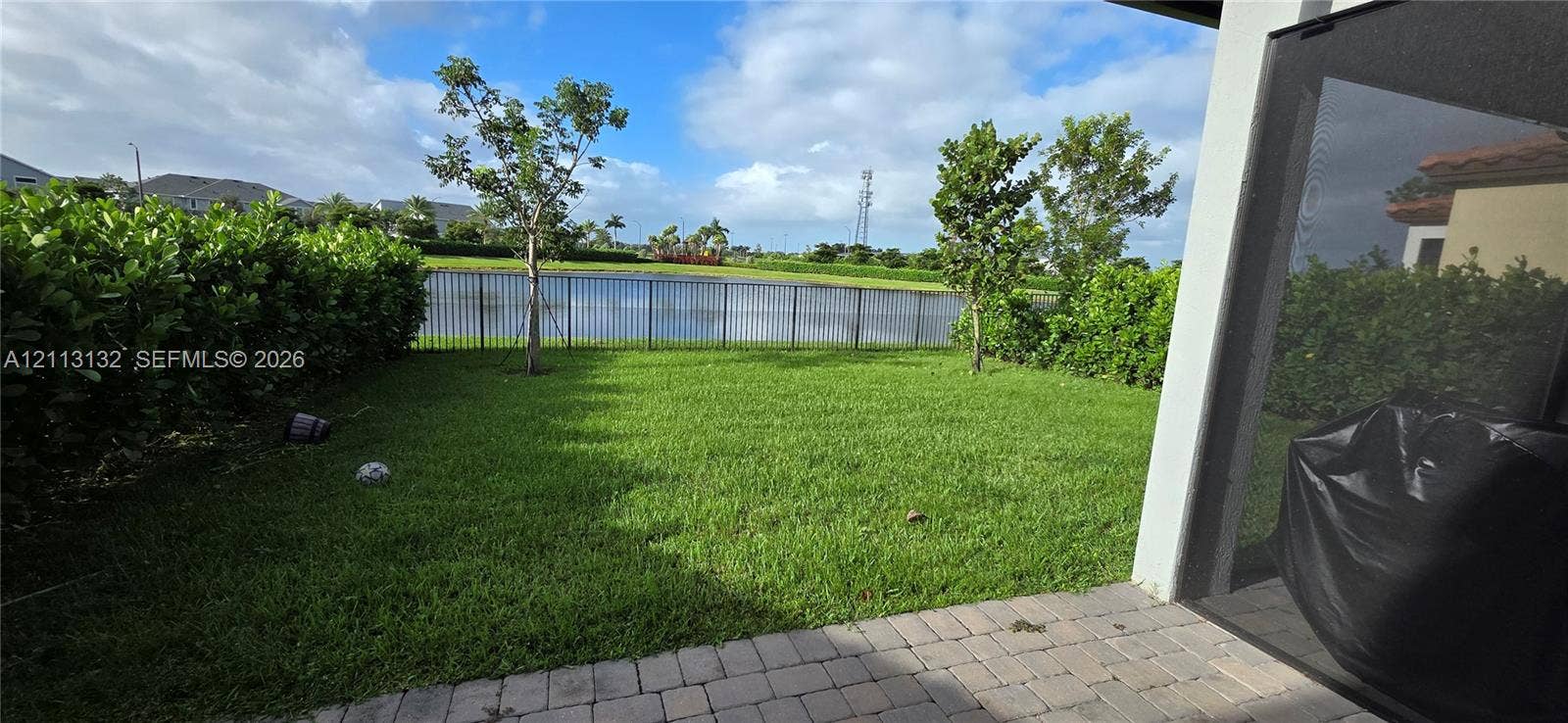 16474 Sea Turtle Place, Westlake, Westlake, FL 33470 Backyard featuring a paved patio, manicured lawn, perimeter hedge fencing, and metal enclosure overlooking a pond