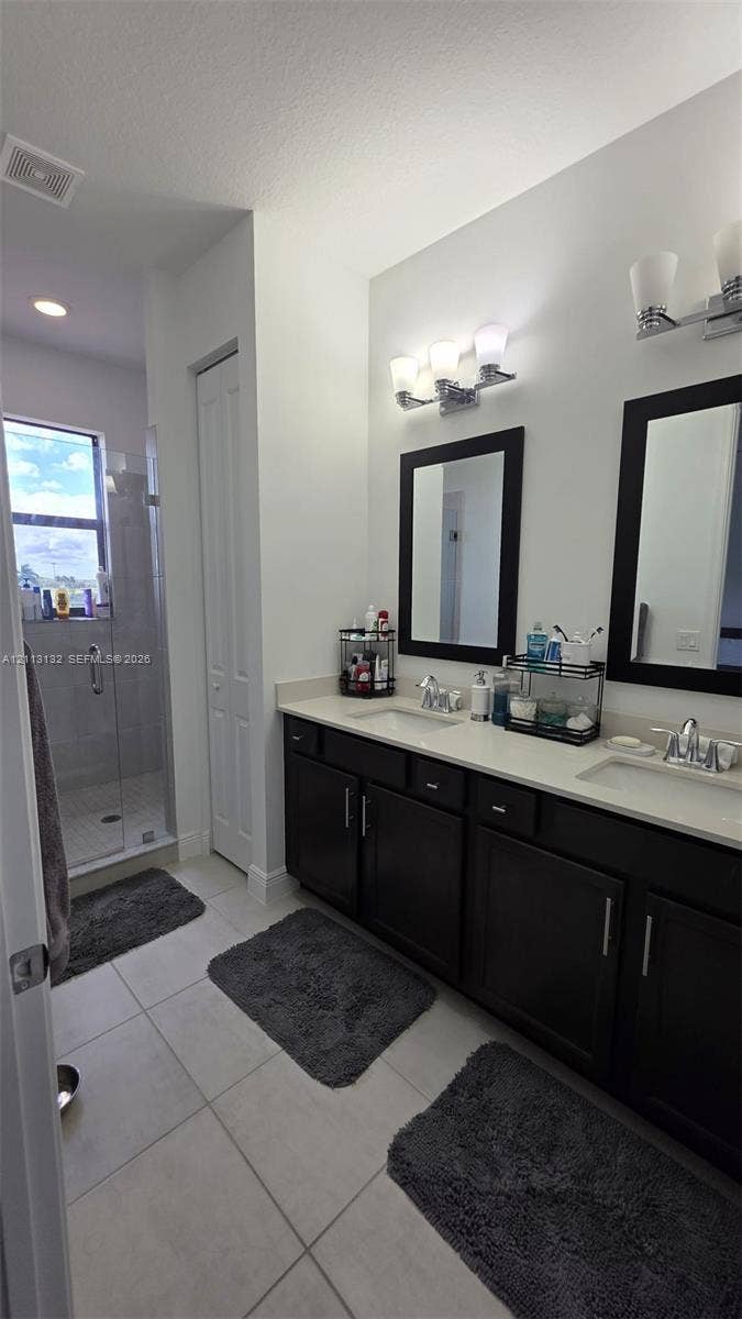 16474 Sea Turtle Place, Westlake, Westlake, FL 33470 Dual vanity with dark cabinetry, light-toned countertop, framed mirrors, and glass-enclosed shower with tile flooring