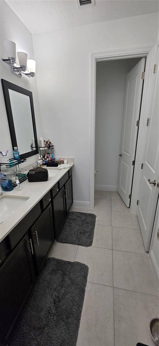 16474 Sea Turtle Place, Westlake, Westlake, FL 33470 Double-sink vanity featuring dark cabinetry, light stone-finish countertops, three-light wall-mounted fixture, and oversized ceramic tile flooring