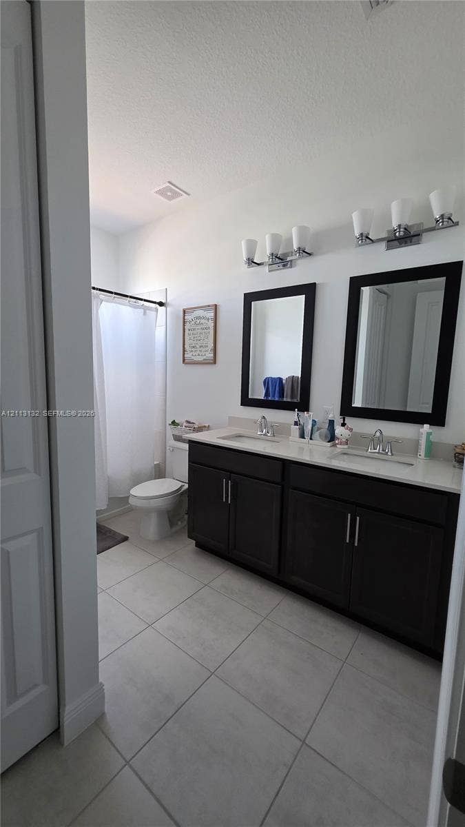 16474 Sea Turtle Place, Westlake, Westlake, FL 33470 Double vanity with dark cabinetry, stone-finish countertops, dual framed mirrors, and large-format neutral tile flooring
