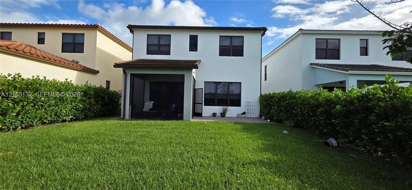 16474 Sea Turtle Place, Westlake, Westlake, FL 33470 Two-story stucco exterior featuring a screened-in rear patio, concrete hardscaping, and a grass lawn enclosed by mature hedges