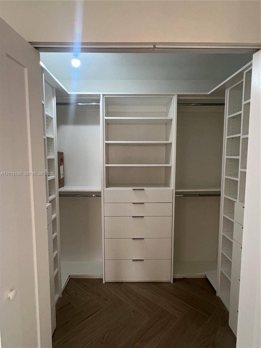 1600 S Ocean Drive, #3A, Hollywood, FL 33019 Walk-in closet featuring white built-in shelving, integrated storage drawers, hanging rods, and herringbone-patterned wood-finish flooring