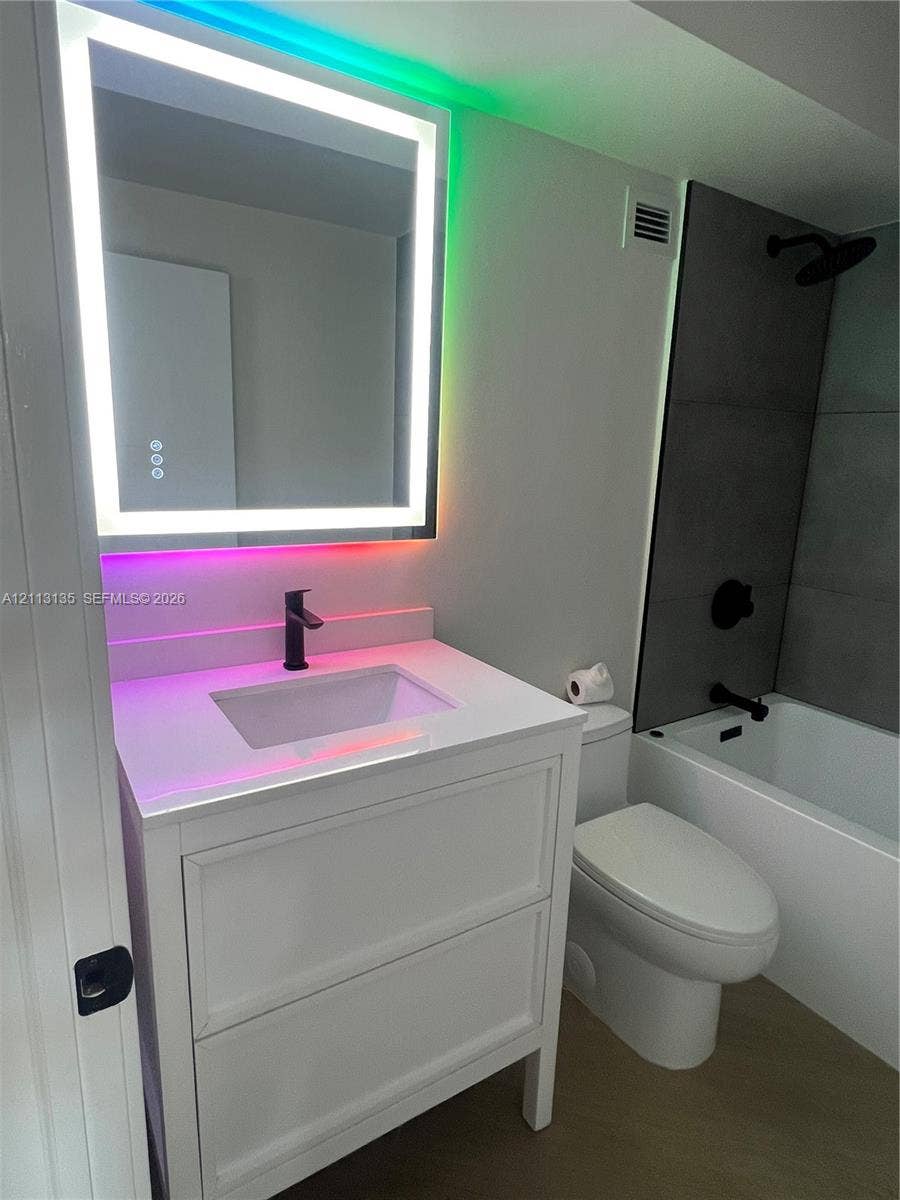 1600 S Ocean Drive, #3A, Hollywood, FL 33019 White cabinetry vanity with a solid-surface countertop and undermount sink, integrated matte black faucet, wall-mounted LED-backlit mirror, and tub enclosure featuring large-format dark tiling with matte black hardware