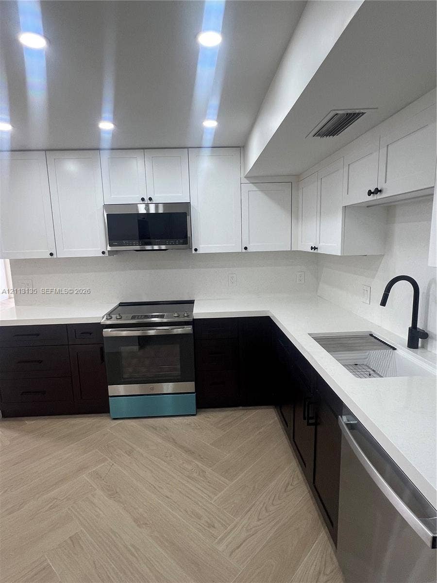 1600 S Ocean Drive, #3A, Hollywood, FL 33019 Kitchen featuring two-tone cabinetry, white stone-composite countertops, stainless steel appliances, matte black hardware, and wood-finish herringbone flooring