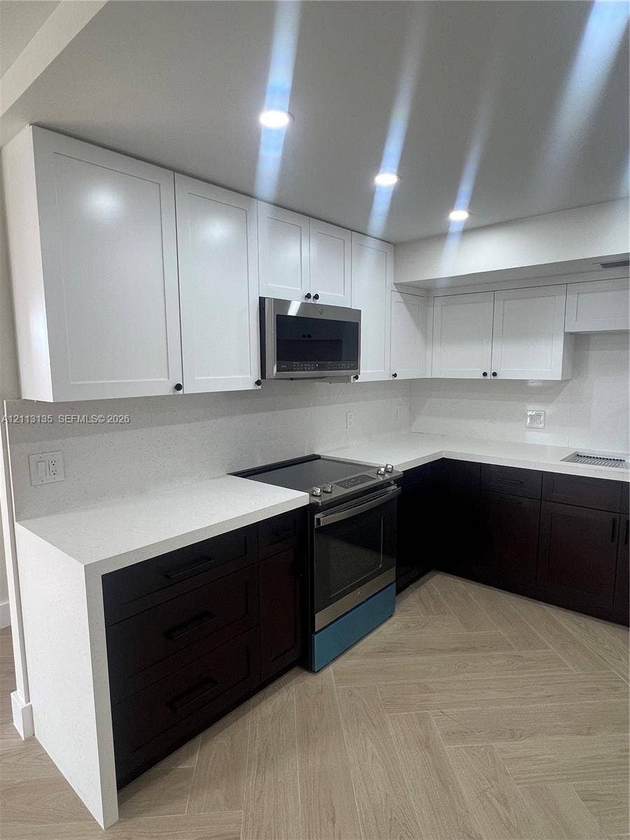 1600 S Ocean Drive, #3A, Hollywood, FL 33019 Two-tone cabinetry featuring white upper cabinets and dark lower drawers, solid surface countertops, stainless steel over-the-range microwave, electric range, and wood-finish flooring in a herringbone pattern