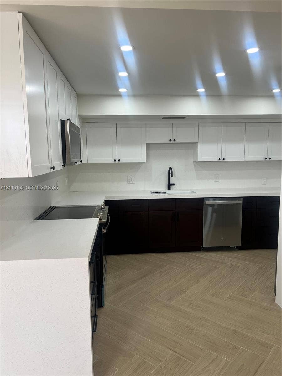 1600 S Ocean Drive, #3A, Hollywood, FL 33019 Kitchen featuring white upper cabinetry, dark base cabinetry, solid surface countertops, a matte black faucet, and wood-finish herringbone flooring
