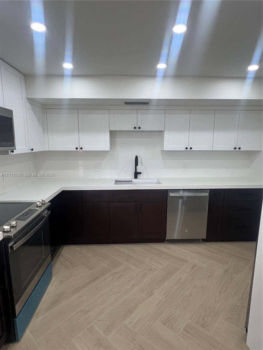 1600 S Ocean Drive, #3A, Hollywood, FL 33019 Kitchen featuring two-tone cabinetry, solid surface countertops, a matte black faucet, integrated stainless steel appliances, and herringbone-pattern wood-finish flooring