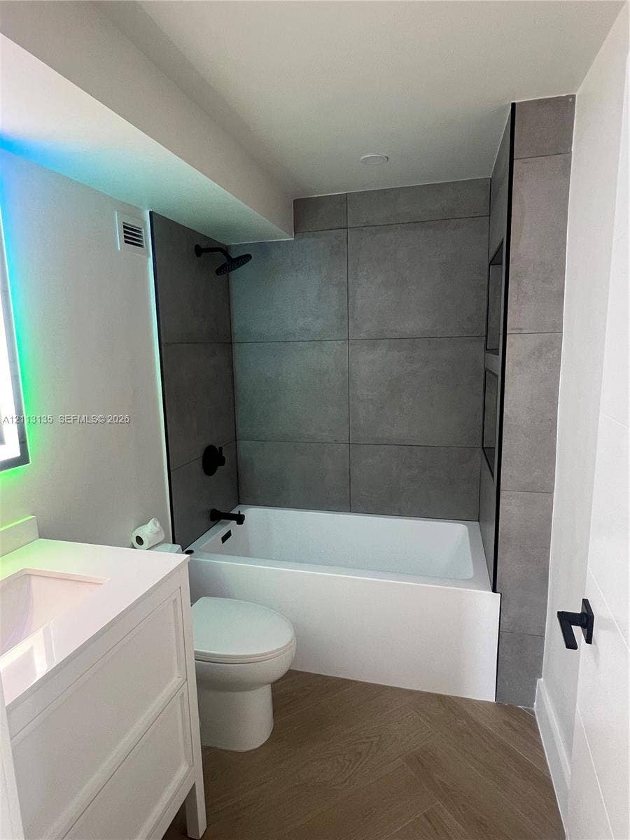 1600 S Ocean Drive, #3A, Hollywood, FL 33019 Bathroom featuring large-format gray tile shower surround with integrated shelving, white vanity with rectangular basin, matte black fixtures, and herringbone-patterned wood-finish flooring